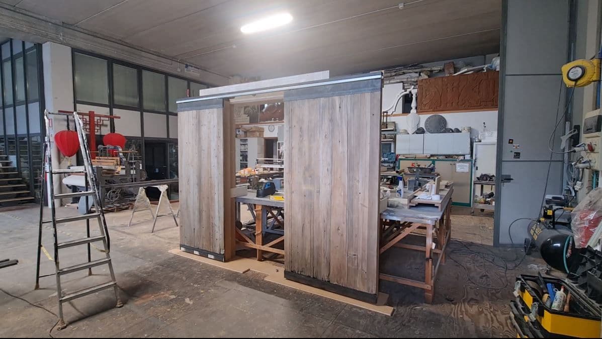 Coppia di porte scorrevoli in legno grezzo posizionate sul telaio di prova all'interno dell'officina.
