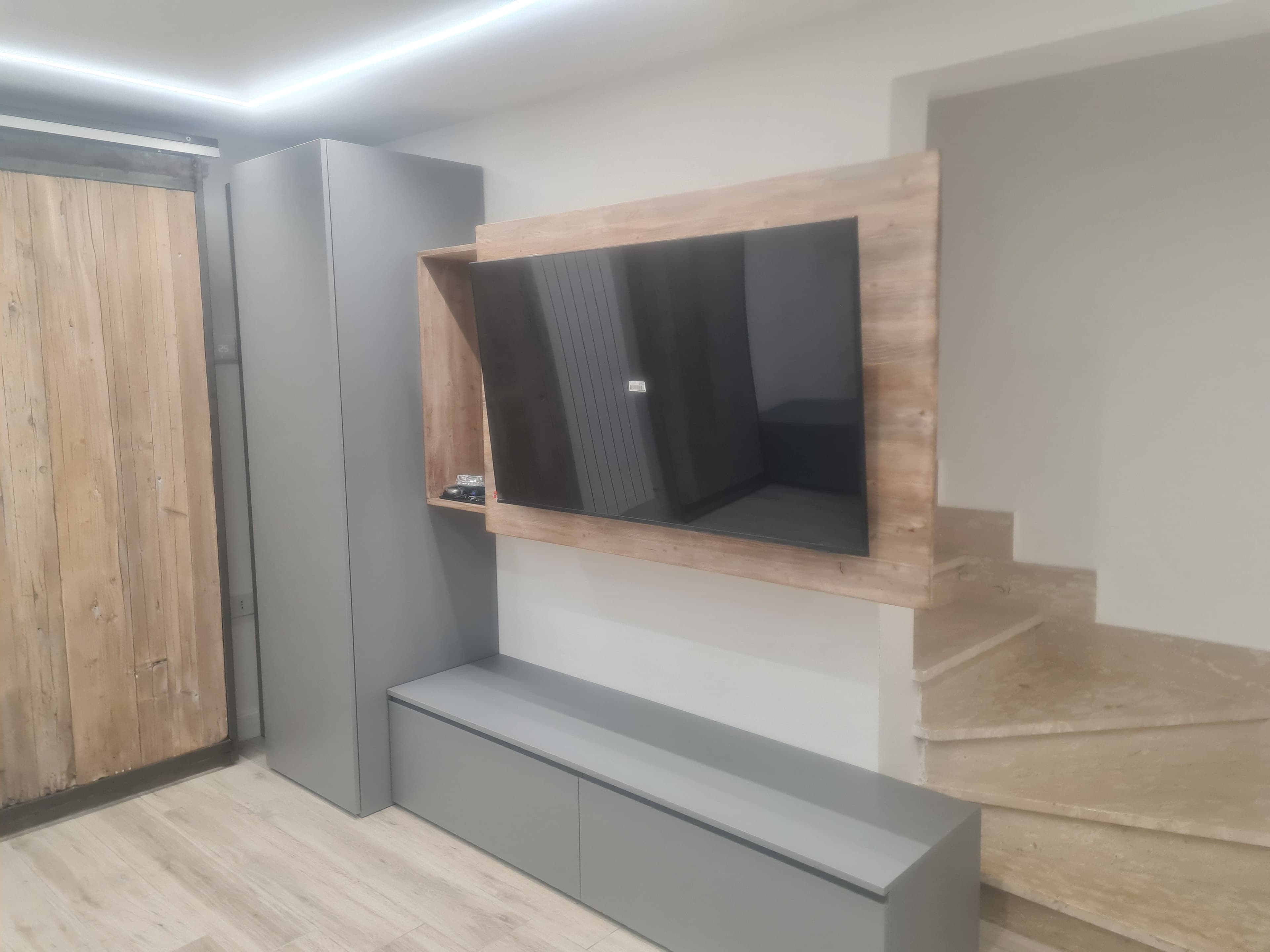Mobile TV su misura nei toni del grigio con pannello di supporto in legno e vani contenitori.