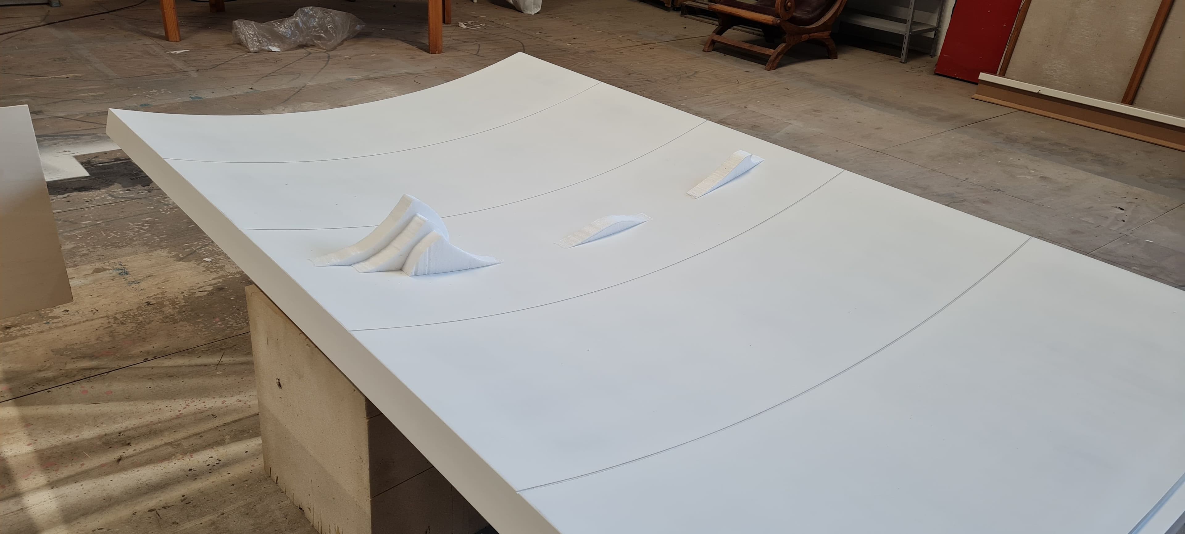 Pannello di legno curvo verniciato di bianco steso nel laboratorio con piccoli elementi tridimensionali applicati.