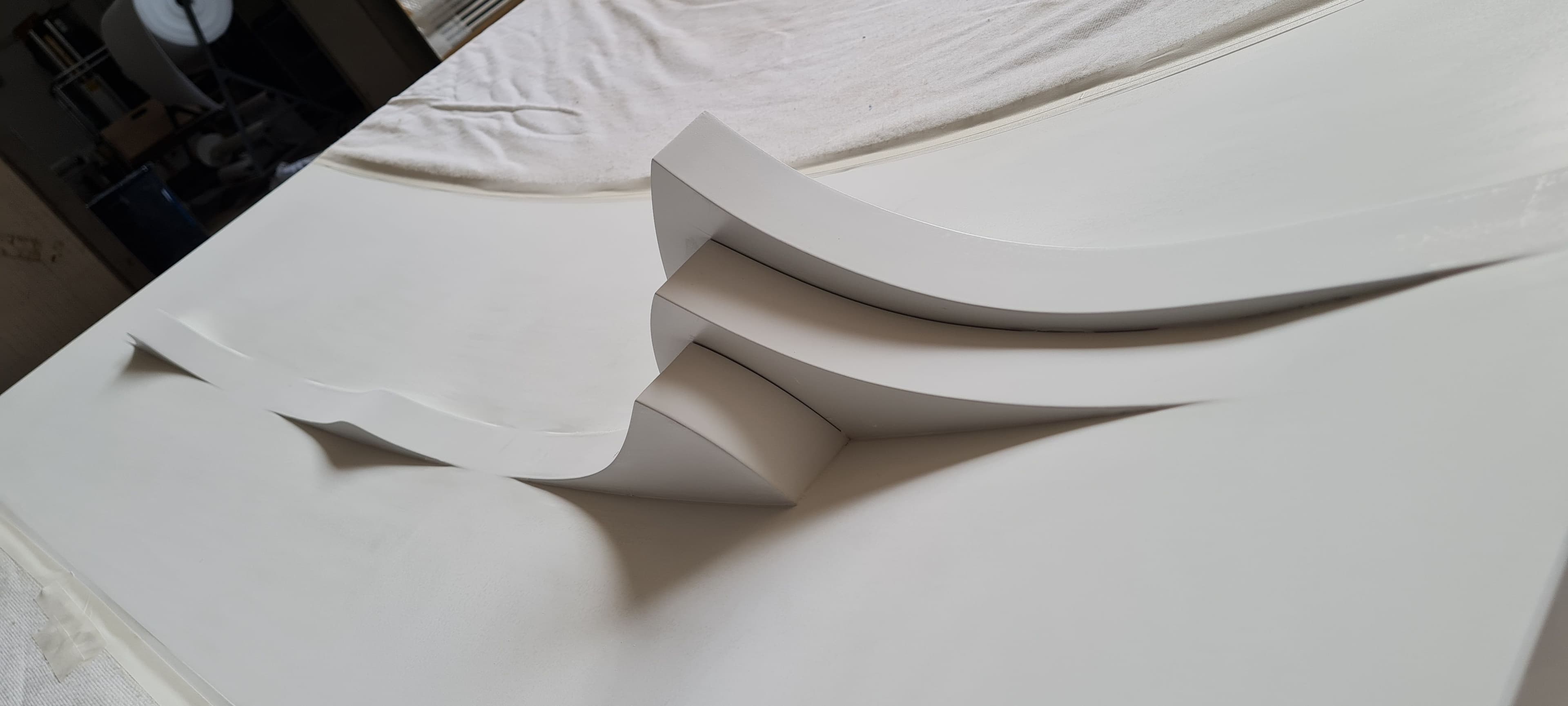 Primo piano del dettaglio scultoreo tridimensionale con linee fluide e finitura bianca omogenea.